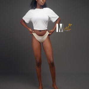 A model wearing a white crop top and nude Abeni brief underwear poses while adjusting the waistband, showcasing confidence and style.