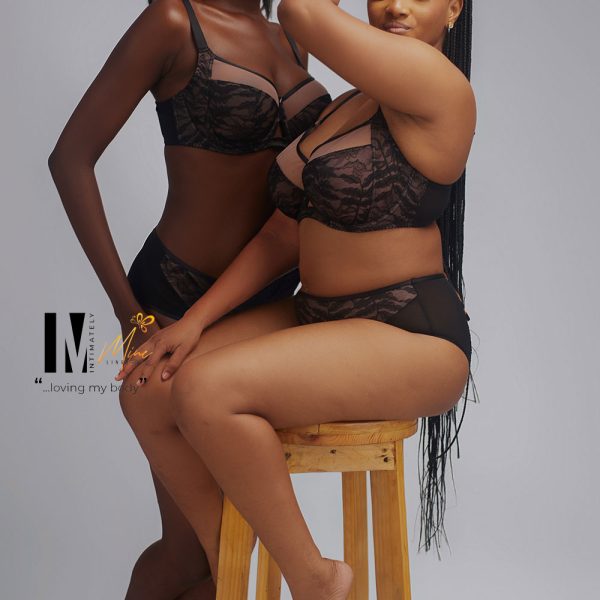 Two women pose confidently on a wooden stool, wearing elegant black lingerie with lace details, showcasing body positivity and confidence.